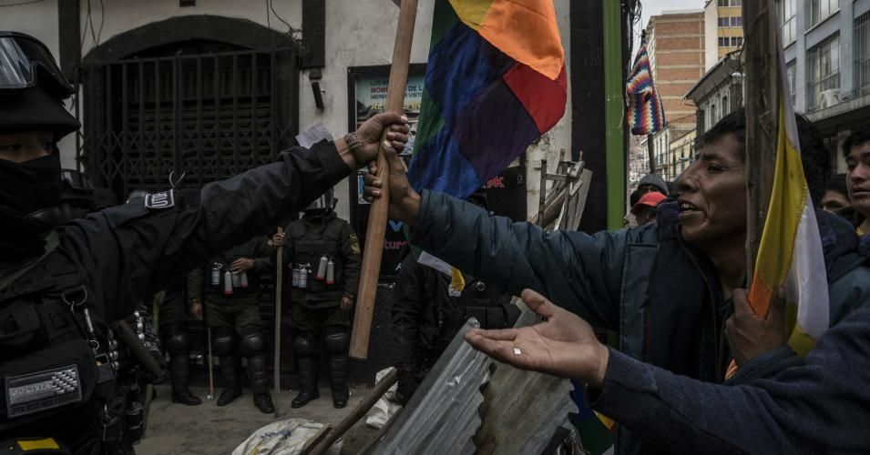 A supporter of former President Evo Morales hands over an indigenous flags "wiphala" to an anti-riot police officer during a protest in La Paz, Bolivia, on November 12, 2019. Protesters have been in the streets calling for Morales' resignation. He stepped down after the army requested he leave his post and requested political asylum from Mexico. (Photo: Marcelo Perez Del Carpio/Anadolu Agency via Getty Images)