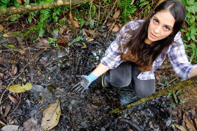 In the Pozo Aguarico region of Ecuador, lawyer Maria Cecilia Herrera shows the oil pollution that remains in the ground 30 years after oil production ceased. Photograph by Enrico Aviles, 2020.