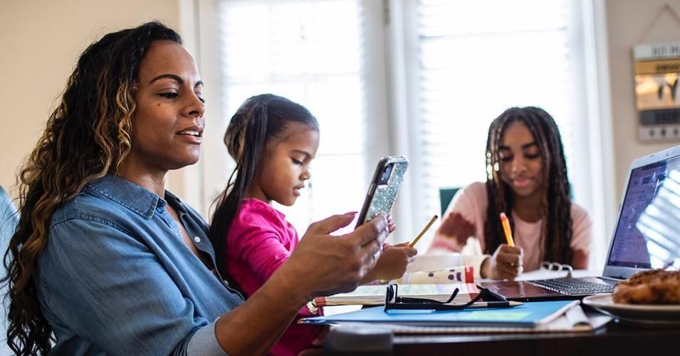 A mother looks at her phone while her daughters do their homework. (Photo: Momo Productions/Getty Images) 