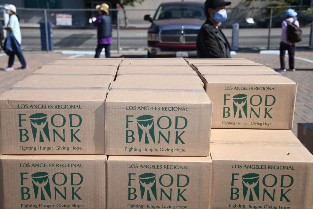 Boxes of food are stacked next to people waiting in line at a walk-up food distribution bank for people facing economic hardship or food insecurity, in a church parking lot in Los Angeles, California, August 10, 2020 amid the COVID-19 pandemic. (Photo by ROBYN BECK/AFP via Getty Images)