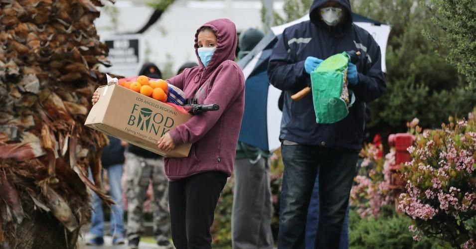 A recipient carries a box of food as others wait in line at a Food Bank distribution for those in need as the coronavirus pandemic continues on April 9, 2020 in Van Nuys, California. (Photo: Mario Tama/Getty Images)