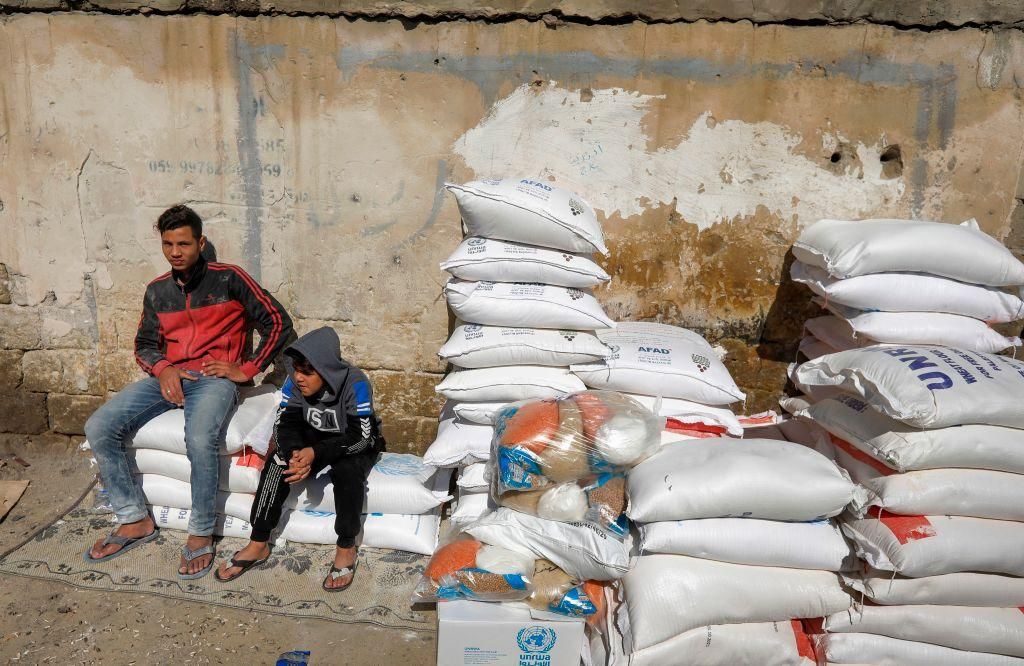 Youths sit next to sacks of flour provided as humanitarian aid by the United Nations Relief and Works Agency (UNRWA) at a distribution centre in the Shati camp for Palestinian refugees in Gaza City on February 21, 2021. (Photo: MAHMUD HAMS/AFP via Getty Images)