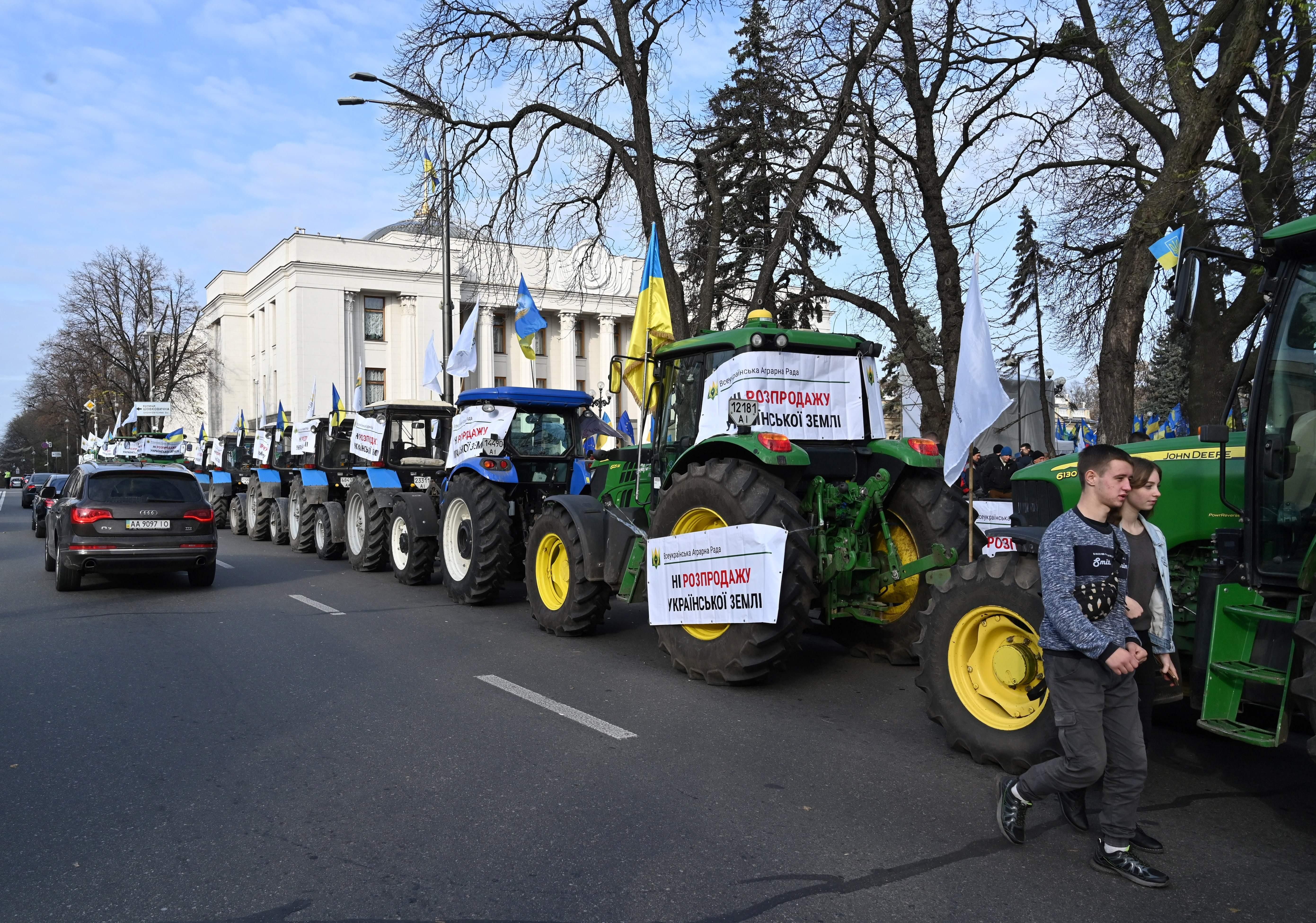 A couple walks along a line of tractors blocking the parliament in Kiev on November 12, 2019, during a rally to protest against government plans to lift the moratorium on agricultural land sales, a step long awaited by investors but opposed by the Ukrainians fearing a foreign land grab. The former Soviet country, whose stalling economy has been propped up by Western aid in recent years, is home to some of the largest swathes of cultivated land in Europe. (Photo by Sergei SUPINSKY / AFP) (Photo by SERGEI SUP