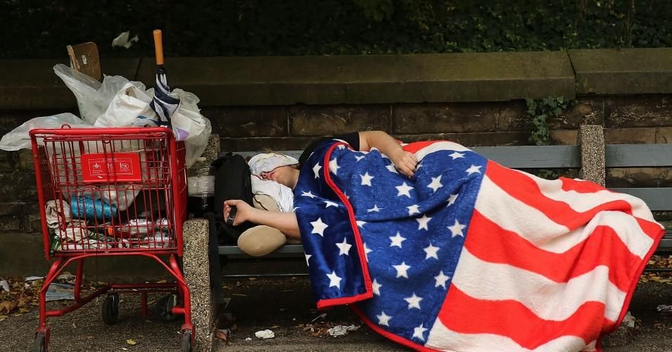 A homeless man sleeps under an American Flag blanket on a park bench on September 10, 2013 in the Brooklyn borough of New York City. (Photo: Spencer Platt/Getty Images)