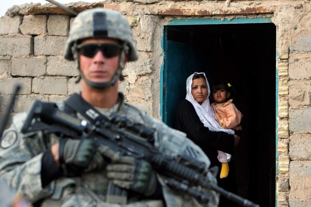 A woman holding her child looks at US soldier from the 4th Battalion, 64th Armor Regiment securing her house during a house to house assessment mission in Baghdad, 09 January 2008. (Photo by JEWEL SAMAD/AFP via Getty Images)