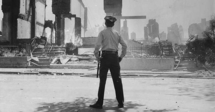 An officer stares at the burnt remains of the MOVE compound in Philadelphia, Pennsylvania. (Archival photo via PBS)