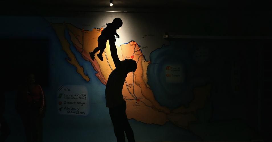  A Honduran immigrant entertains a fellow immigrant's child in front a map of Mexico showing train routes leading north at a shelter for undocumented Central American immigrants on September 14, 2014 in Tenosique, Mexico. The shelter, called La 72, is run by Fransiscan friars and is the first stop for thousands of Central American immigrants crossing north through Mexico to reach the United States. Many risk riding atop "La Bestia" or The Beast, a freight train which passes through Tenosique in Mexico's sou
