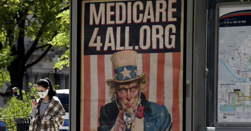 A pedestrian wearing a protective mask checks her phone near a Medicare for All bus stop billboard in Washington, DC, on April 22, 2020. (Photo: Olivier Douliery/AFP via Getty Images)