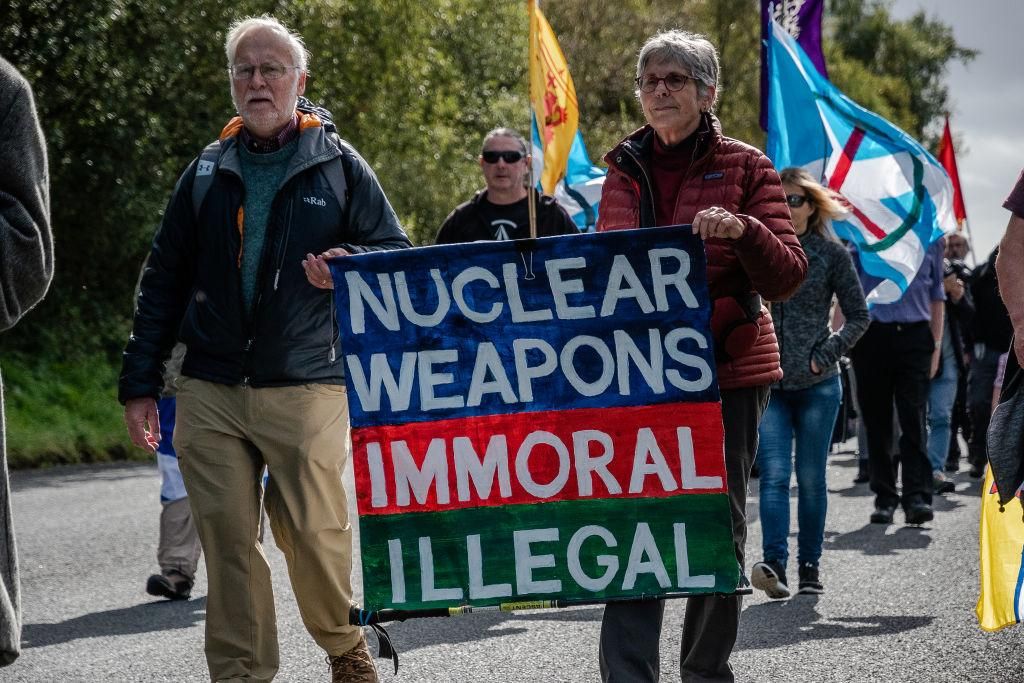 Two protesters are seen holding a sign that reads Nuclear weapons Immoral, Illegal. Various members of different CND, Anti-war and peace campaigners gathered outside HMNB Clyde or Faslane to protest Trident and the bases of nuclear capable submarines. There is a permanent peace camp at the base. (Photo by Stewart Kirby/SOPA Images/LightRocket via Getty Images)