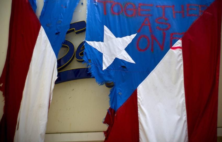 A damaged Puerto Rican flag spray-painted with the words "Together as One" hangs from the facade of a business in San Juan.