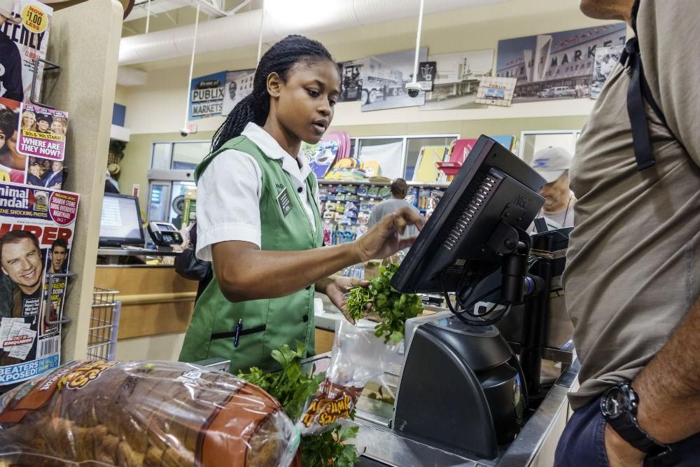 A Publix supermarket cashier. A 2019 Oxfam report shows that raising the minimum wage to $15/hr would benefit 40 million workers and their families. (Photo by: Jeffrey Greenberg/UIG via Getty Images)