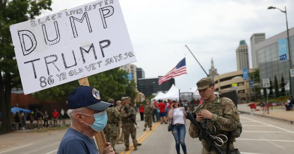 Veteran Richard Saul carries a sign that reads "Dump Trump" as a member of the Oklahoma National Guard stands nearby ahead of a U.S. President Donald Trump campaign rally at the BOK Center on June 20, 2020 in Tulsa, Oklahoma
