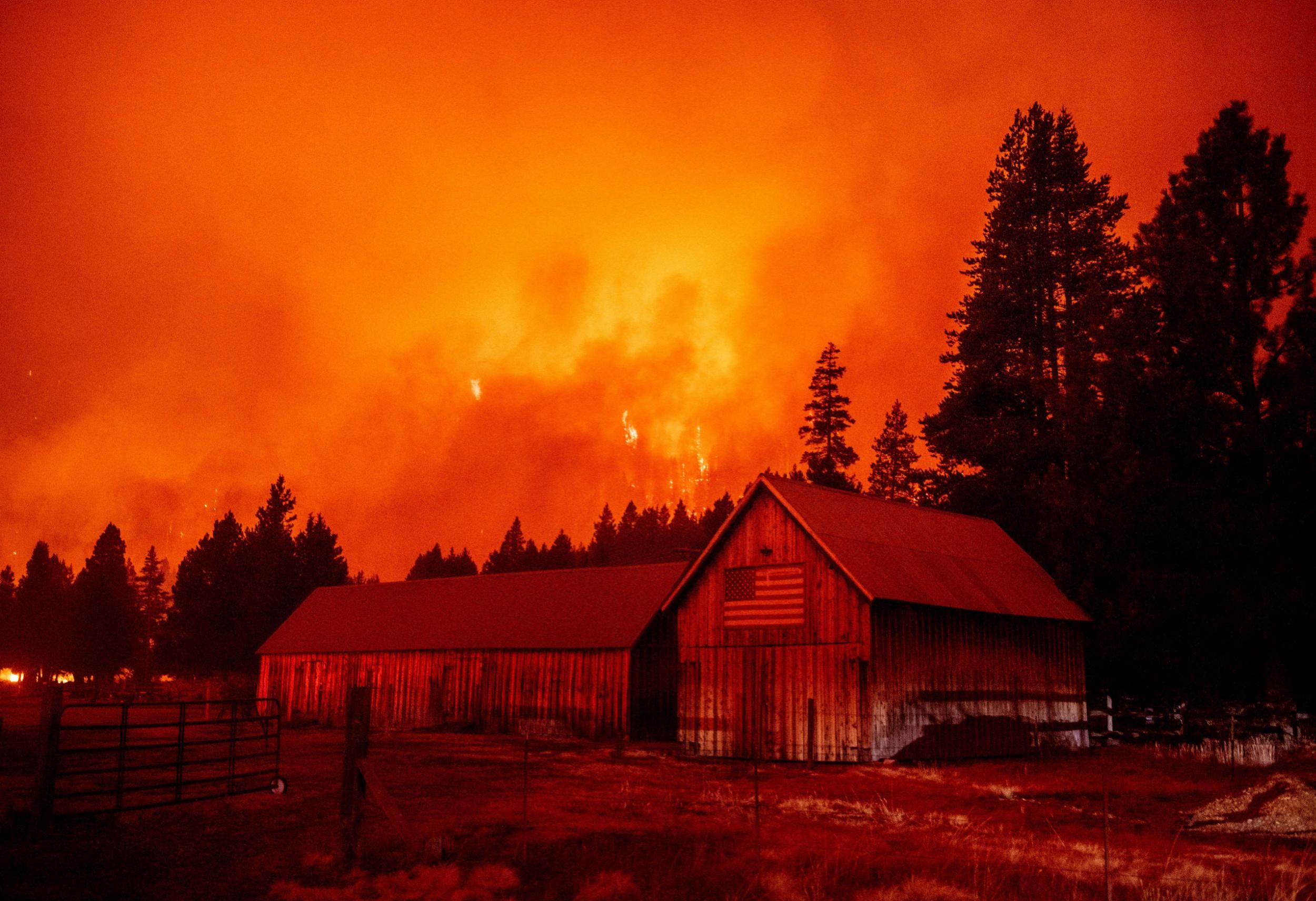 Flames rip across a hillside behind a building donning a U.S. flag as the Caldor Fire pushes into South Lake Tahoe, California on August 30, 2021. (Photo: Josh Edelson/AFP via Getty Images)