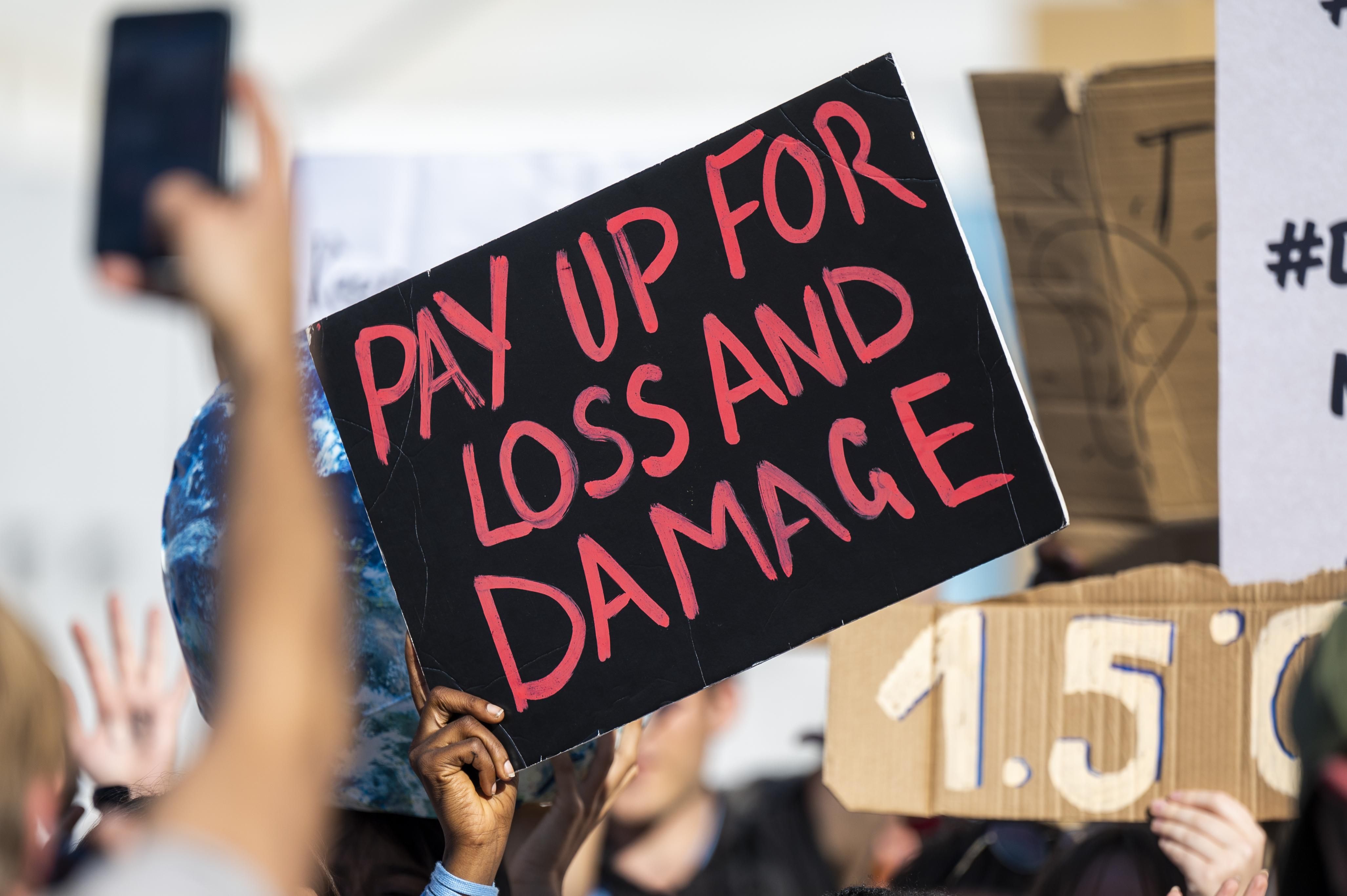 Sign reads "Pay Up for Loss and Damage"